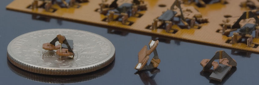 Tiny manufactured objects next to a quarter for scale