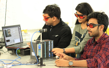 Three students with laptop and optical equipment.