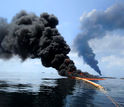 Dark clouds of smoke emerge as a controlled burn of spilled oil takes place on the ocean surface.