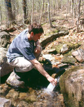 Photo of a scientist collecting a stream sample at the Hubbard Brook LTER Site.
