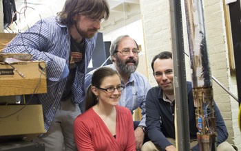 Photo of  researchers examining a tubular structure to measure the magnetic charge of an antiproton.