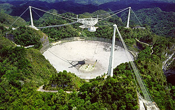 White telescope floats over concrete crater, lush hills in background.