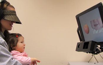 Photo of a 10-month-old baby held by a woman watching images on a monitor.