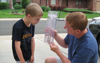 man and child look at a rain gauge in a driveway