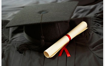 Photo of a degree adjacent to a graduation cap on a black cloth.