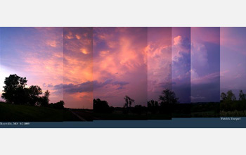 Photo of a storm in the background and trees in the foreground.