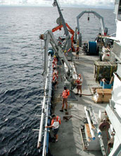 Team of men deploying a core barrel from a research vessel at sea.