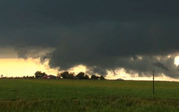 Storm cloud over a field with a house and other structures in the background