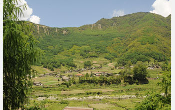 Photo of farms with forest-covered hills in background.