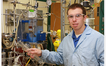 Photo of Edward Kunkes in the lab next to a reactor system used to convert sugar to gasoline.