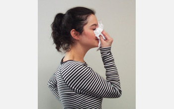 Photo of a woman blowing her nose into tissue.