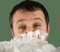 Photo of a man with a cold with a pile of tissues in front of him.