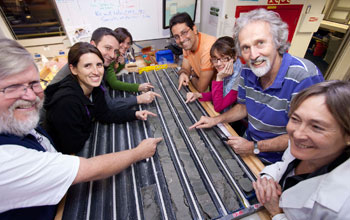 Photo of members of the expedition science party looking at a core sample in a shipboard lab.