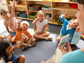 Photo of a teacher holding cards with letters and kindergarten students raising their hands.