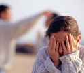 Photo of boy covering his eyes with his hands with two people in the background.