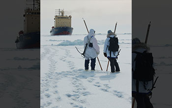 Two people on sea ice in north Bering Sea hold Arctic native ice-testing sticks called unghaqs