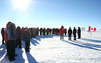 A memorial ceremony at South pole showing people gathered on the ice and the Canadian flag.