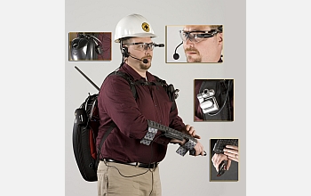 A man wears a back pack with a keyboard, camera, video viewer and microphone attached to him.