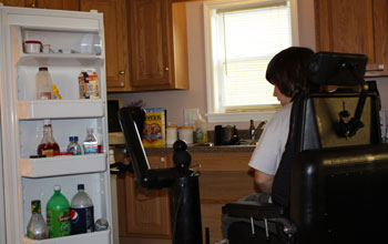 Photo of a disabled person piloting a robotic mobility and manipulation system to open frig door.