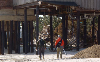 Tow scientists walking on the beach under houses to study erosion from Sandy