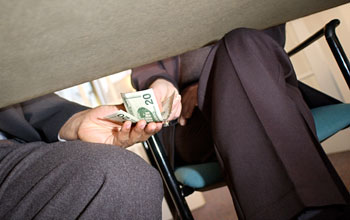 Photo of a man handing two twenty dollar bills to another man beneath a table.