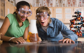 two school children with their mouths open looking at a liquid- and gas-filled flask .