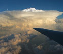 Photo of a plane wing in the foreground and clouds in the background.