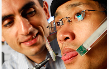 Photo of Maysam Ghovanloo (left) pointing to a small magnet attached to tongue of graduate student.