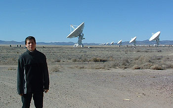 Young man stands in front of a row of white telescopes.