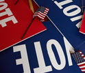 Photo of a pile of red and blue VOTE signs.