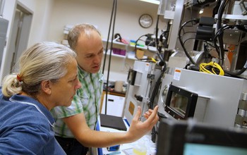 Matthew White and a visiting researcher discuss the features of the dual-vacuum-chamber solar cell fabrication facility at the University of Vermont.