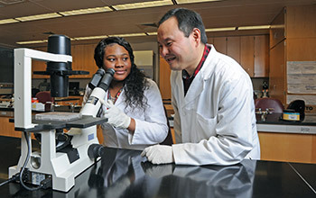 Two people in lab coats next to a microscope.