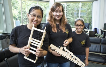 Three Middle School Academy students with parts of a balsa wood bridge they built