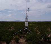 A tower placed on desert ground, with mountains in the background.