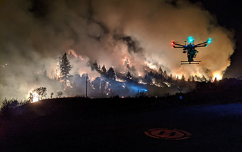 A drone hovers over its flight pad on the perimeter of a prescribed burn