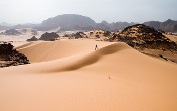 Man walking up sand dune in the Sahara Desert.