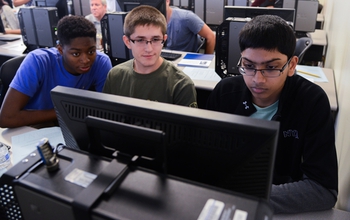 three students at a computer part of a cybersecurity camp