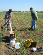 Two scientists install a weather station in an agricultural field.