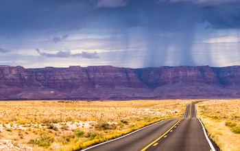 View of clouds, mountains, flatlands, and two-lane road during an intense rainstorm in Arizona.