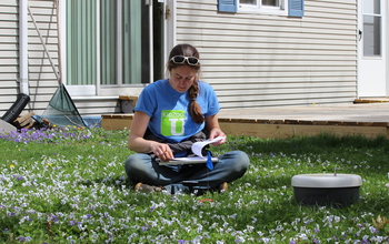 Female scientist sitting in grass, holding notepad and pencil.