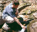 Photo of a scientist collecting a stream sample at the Hubbard Brook LTER Site.