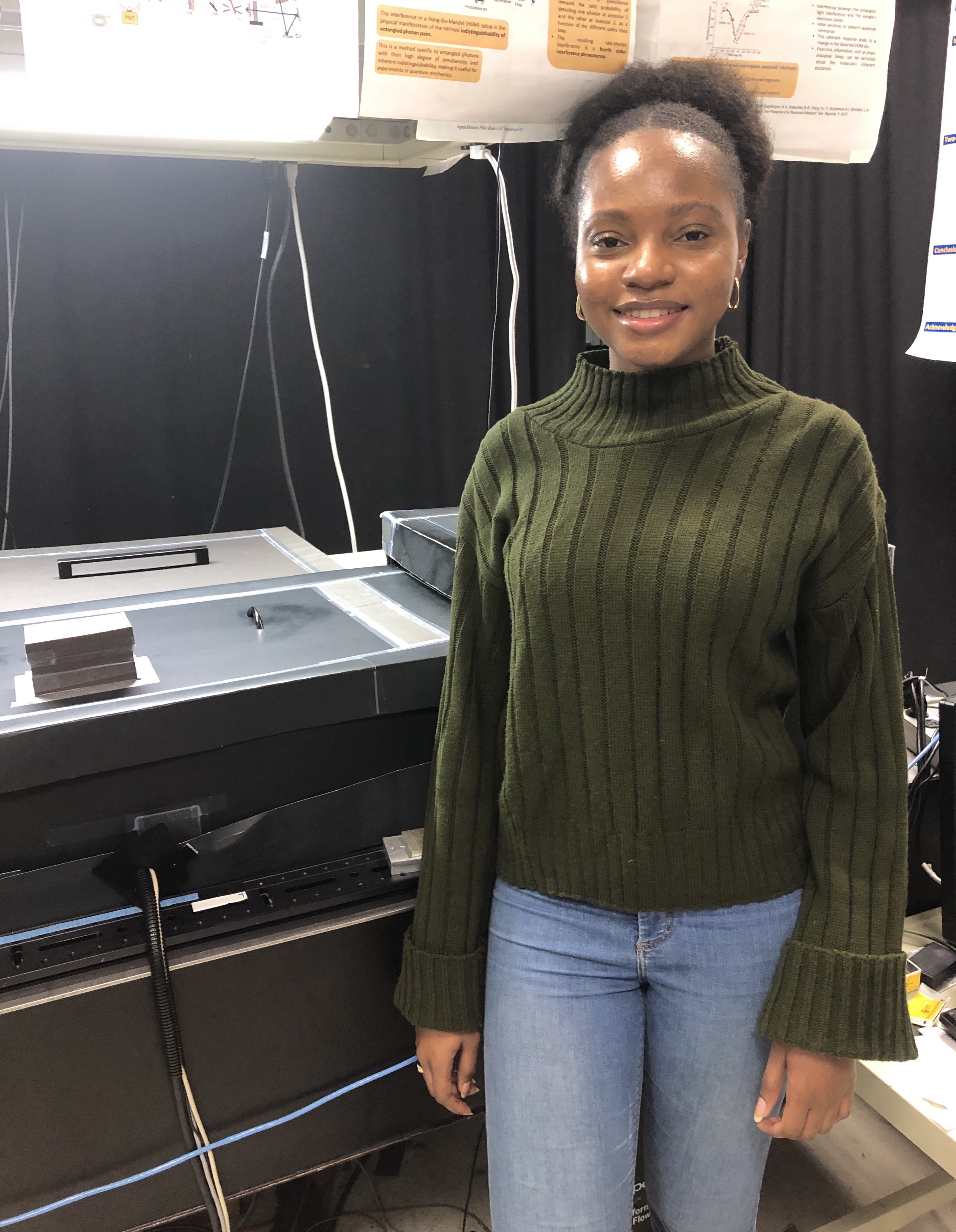 Audrey Eshun, Ph.D. Candidate in Quantum Science, standing beside her laser setup at the University of Michigan.