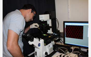 Photo of a scientist pipetting a sample onto a slide on a microscope stage.