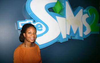 A young woman standing in front of a sign with the text The SIMS.