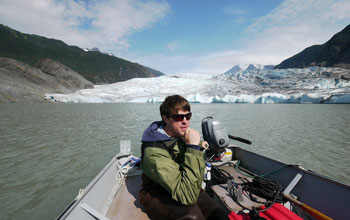 Photo of researcher Eran Hood operating the motor in a boat with Mendenhall Glacier in background.
