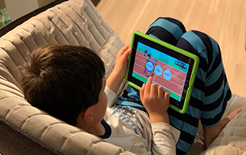 little boy sitting on a sofa playing with a tablet