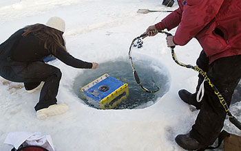 Photo of two people lowering a device into a hole in the ice.