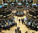 Photo of people walking and viewing computer monitors on the stock market floor.