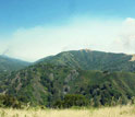Photo of forest covered hills in western U.S. wildfire with smoke from wildfires in distance.