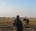 Photo of a herder standing in front of his family's encampment and cattle.